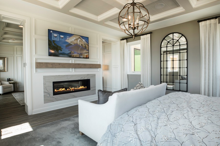 Fireplace with TV mounted on top of it, sits in front of a white sofa and bed with gray duvet.  