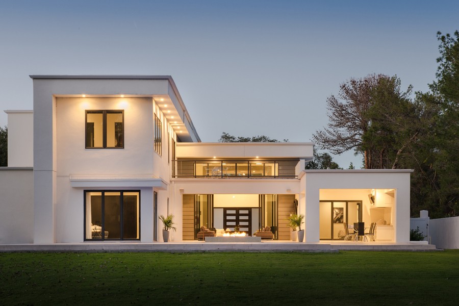 A white home with a modern architectural style showing well-lit interiors and exteriors.