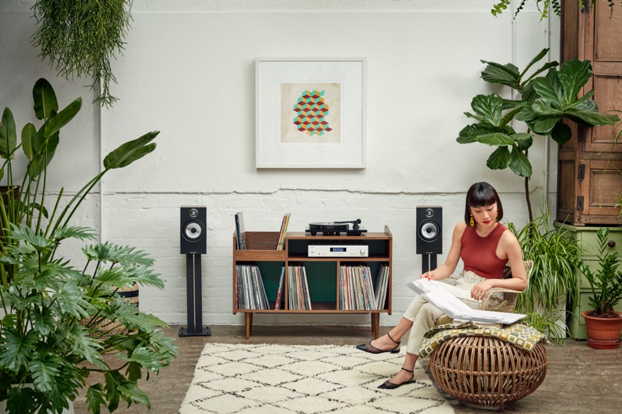 The interior of a listening room featuring a turntable and Bowers & Wilkins speakers with a woman sitting in front of the system while looking at an album’s cover.