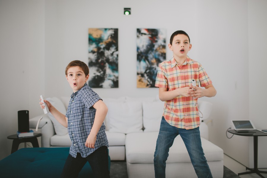 Two young kids in jeans and button down shorts standing in the living room while holding Nintendo Wii remotes and aiming them at the screen. 