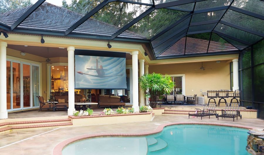 An outdoor area with a Screen Innovations projection screen between the pool and seating area.