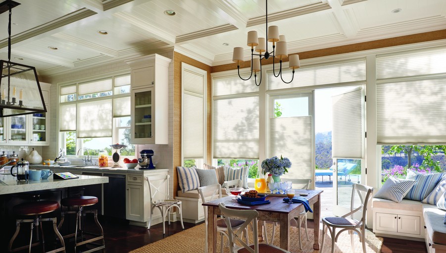 A living room and kitchen with lots of natural lighting. Hunter Douglas motorized shades cover the windows.