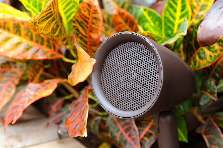 Outdoor landscape speaker by Origin Acoustics nestled among vibrant Croton plants, blending high-fidelity sound with natural garden aesthetics.
