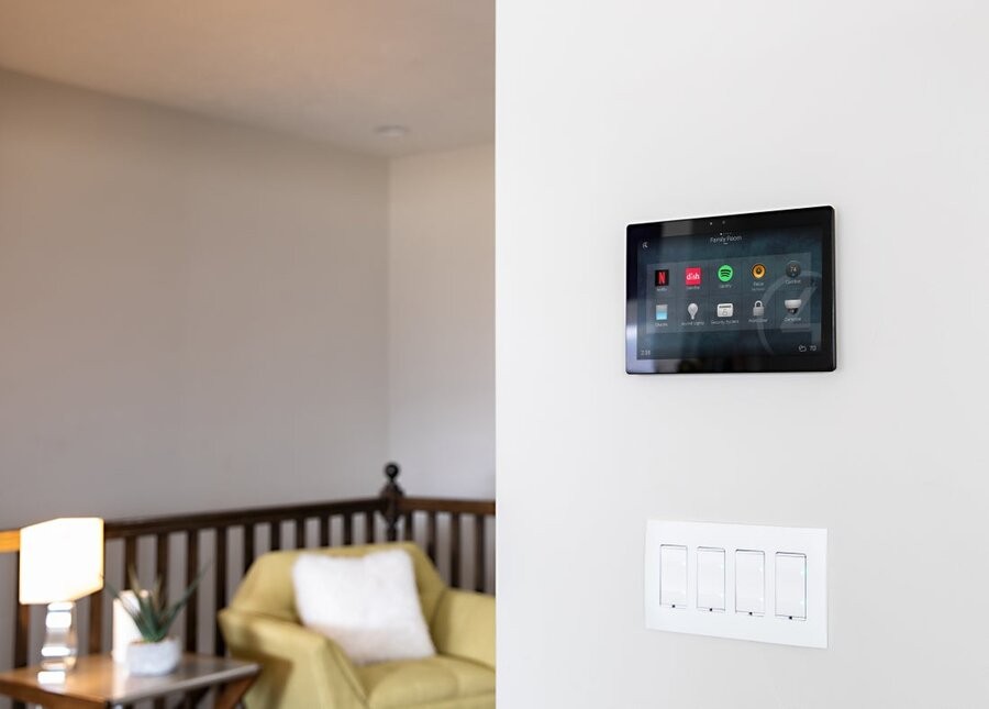 A Control4 wall tablet in focus with a living space in the background.